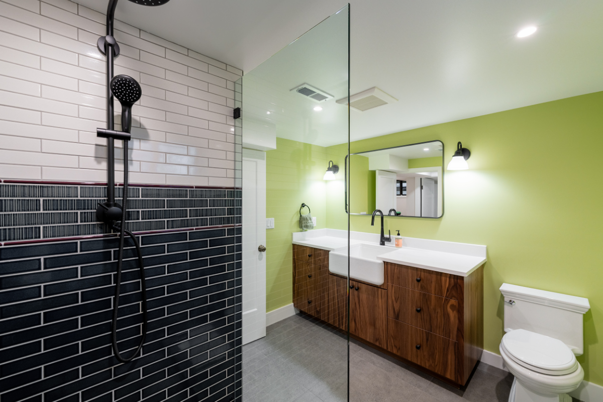 Modern bathroom remodel featuring a glass walk-in shower with black subway tile, wood double vanity, and green walls.